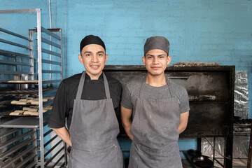 Portrait of two young Hispanic bakers posing in front of the bakery oven
