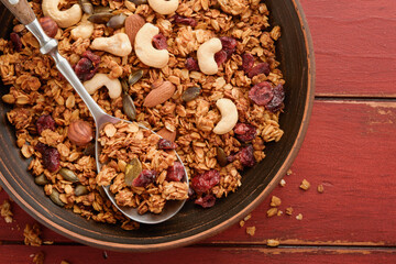 Homemade granola with greek yogurt or milk and cashews, almonds, pumpkin with dried cranberry seeds in old bowl on red rustic wooden table background. Healthy energy breakfast or snack. Top view.