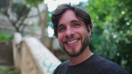 Portrait of handsome young man in his 30s turning head toward camera while holding phone and standing in city park