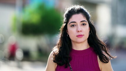 Portrait of a young woman turning head with stoic surprise toward camera standing outside with...