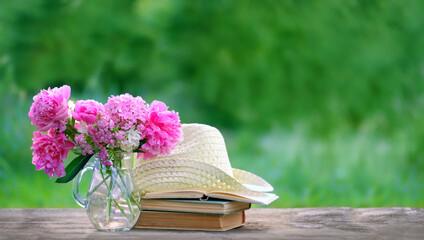 Pink flowers bouquet, books  and braided hat on table in garden, abstract natural background....