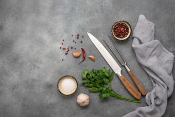 Fototapeta na wymiar Culinary background, knife, meat fork, spices and greens. Gray concrete background. Top view, flat lay, copy space, banner.