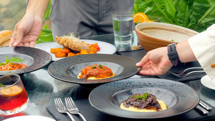 Guests at a luxury resort restaurant are served by a waiters at a table with a tropical view. The elegant setting adds to the romance of the dining experience.