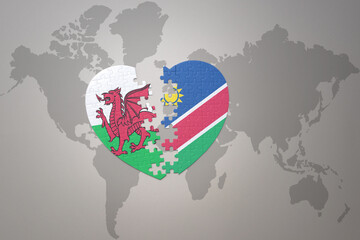 puzzle heart with the national flag of namibia and wales on a world map background.Concept.