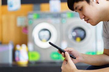 Asian man using smartphone for social networking or chatting with a friends while waiting for...