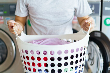 Asian man putting an used or dirty clothes in the self-service automatic laundry washing machine,...