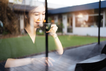 Happy cheerful Asian beautiful woman sitting in the coffee shop in front of the window and working on digital tablet and laptop - notebook computer. Modern working lifestyle concept.