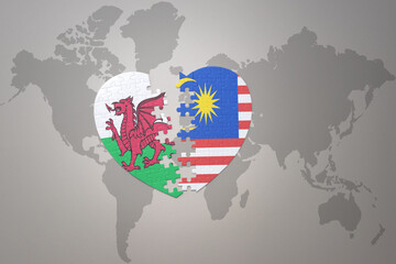 puzzle heart with the national flag of malaysia and wales on a world map background.Concept.