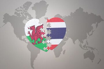 puzzle heart with the national flag of thailand and wales on a world map background.Concept.