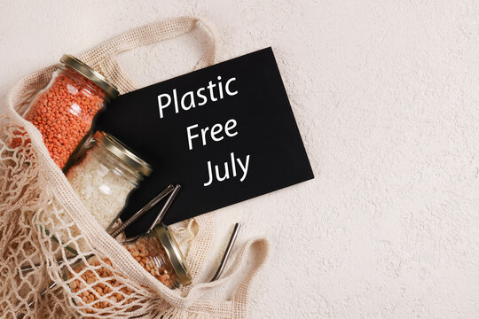 Zero waste lifestyle concept. Responsible consumption. Plastic free July written on black board with mesh , glass jar, reusable straws