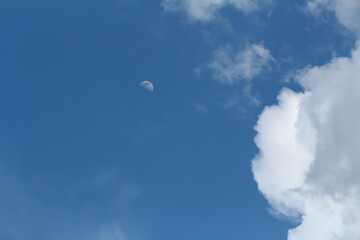 Blue sky with clouds. Spring or summer background. The moon is visible among the clouds.