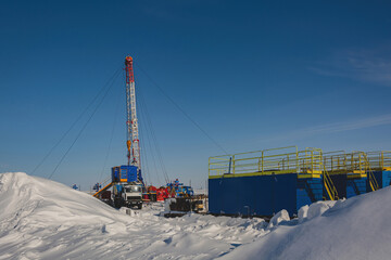 The Northern gas field. There is a lot of snow in the foreground. In the background is a mobile installation for well repair. A frosty winter day. Sunny blue sky