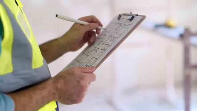 Concentrated man reads project plan of office interior renovation on clipboard in hands professional specialist in uniform studying information standing in unfinished premise