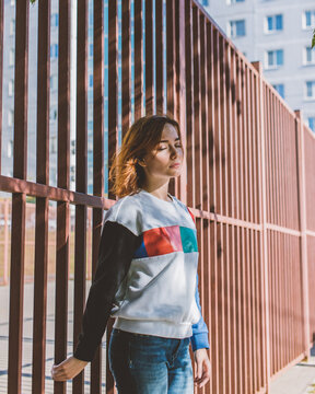The girl is standing with her back to the fence with her eyes closed