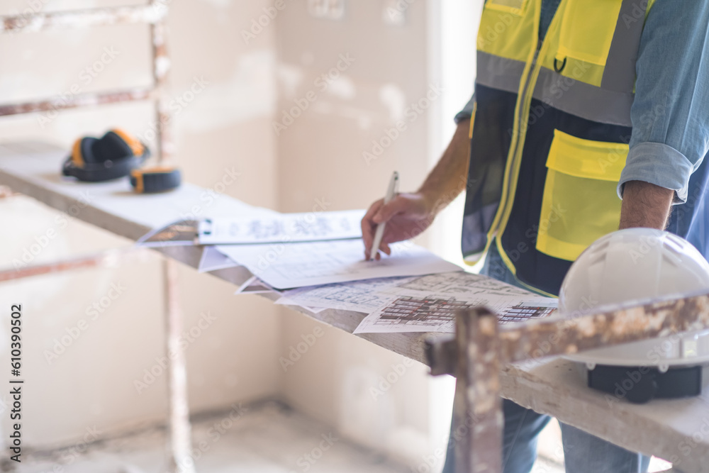 Wall mural worker in professional uniform editing and correcting construction documentation standing in room wi