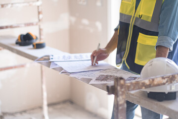 Worker in professional uniform editing and correcting construction documentation standing in room with safety equipment renovation process in apartment