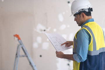 Architect in uniform pointing index finger to project plan stands in unfinished office specialist inspecting premise before starting renovation process construction safety concept and equipment