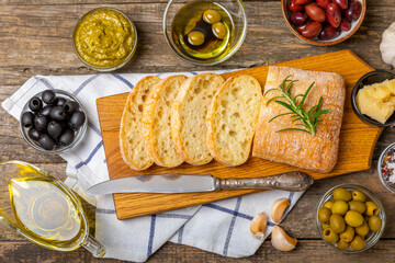 Italian ciabatta bread cut in slices with herbs, olives, pesto sauce, garlic and parmesan cheese on a wooden table. Fresh homemade Italian Ciabatta bread sliced with herbs and spices.Place for text.  - obrazy, fototapety, plakaty