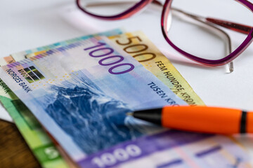 Norwegian krone money on the desk next to Women's Glasses, a white sheet of paper and a pen, Concept, Payment of bills, installments and credits, rising household budget costs in Norway