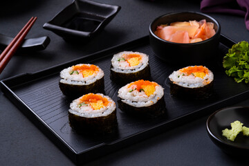 Maki sushi on black tray.Japanese sushi rolls with salmon, cucumber, shrimp eggs and Imitation Crab Stick with soy sauce dip and chopsticks on black table background.