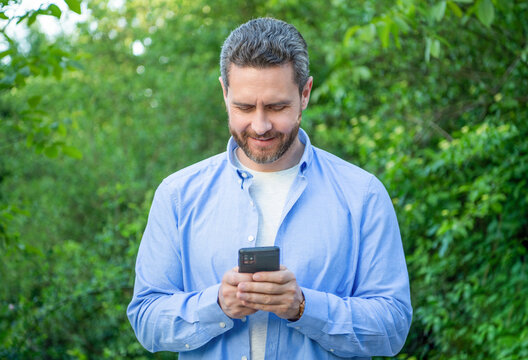 Positive Man Messaging On Phone Outdoor. Man Messaging On Phone Or Checking Email.