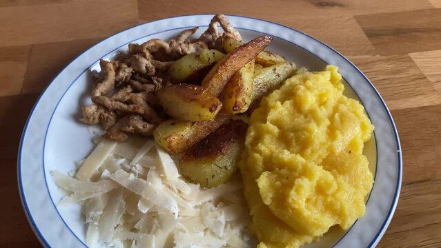 Video of a plate of food containing pork, parmesan cheese polenta and potatoes.