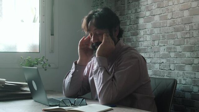 Migraine headache symptoms at home office. One worker adult man stop work on computer sitting at the table for stress. Overworked stressed male people with head ache taking off glass and touch head