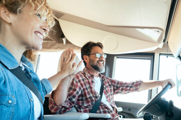 Happy couple celebrate travel day in high five gesture smiling and looking at the road inside a modern camper van. Renting recreational vehicle. People in vanlife happiness lifestyle. Tourism leisure