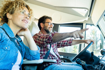 Fototapeta na wymiar Happy couple of adult man and woman driving inside a camper van and enjoying alternative vehicle vacation together. Motorhome travel lifestyle and vacation on the road. People living adventure trip