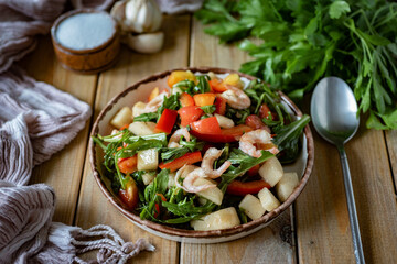 An exquisite dish for a romantic breakfast: salad with shrimp, arugula, fresh tomatoes and olive oil in a beautiful plate on wooden boards. Close-up