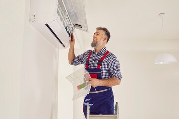 Professional mature bearded electrician man maintaining, cleaning or changing filter in modern air...
