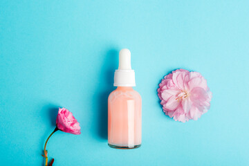Obraz na płótnie Canvas Serum bottle and pink sakura blossom on blue background. Skin care, beauty treatment concept. Top view, flat lay
