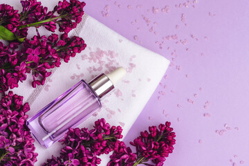 Serum bottle and lilac flowers on light purple background. Natural cosmetics, skin care concept....