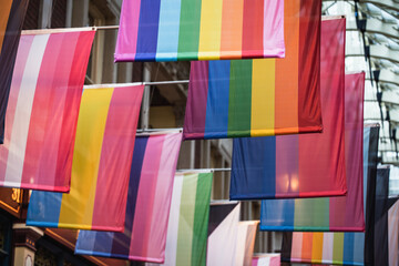 Different LGBTQ pride and rainbow flags hanginging in two rows in city arcade. London