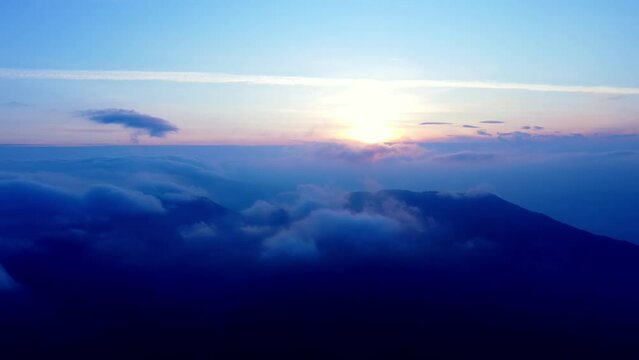 Aerial view forward over the morning clouds with the rising sun in the distance