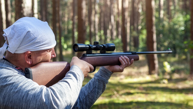 Shooting in the forest from an air rifle with an optical sight. Sunny summer day, back view.