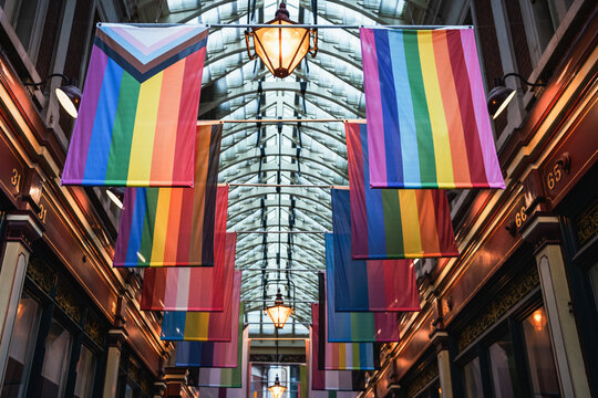 Different LGBTQ pride and rainbow flags hanginging in two rows in city market space. London