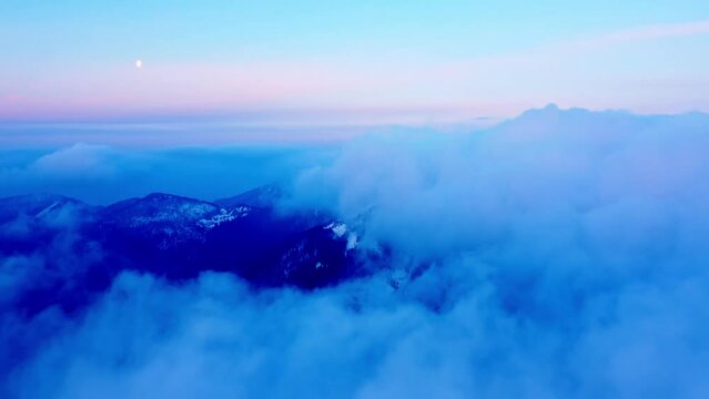 Low aerial view of morning flight over clouds and hills in the mountains ,blue hour before sunrise.