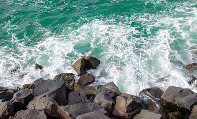 Black stones on bright blue sea waves, summer background. 