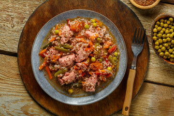 Israeli couscous with sumac chicken pieces and vegetables in a plate on a wooden round stand next to a fork.