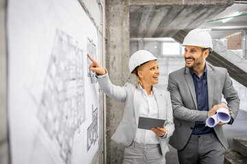 Civil engineers working together at construction site, controlling and inspecting building process. Looking at project plan and blueprint.