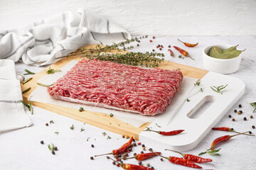 Board with fresh minced meat, thyme, chili peppers and peppercorns on white grunge background