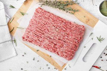 Board with fresh minced meat, thyme and peppercorns on white grunge background