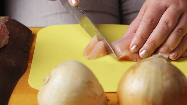 Women's hands cut chicken for cholent with a large knife on a plastic board. close-up