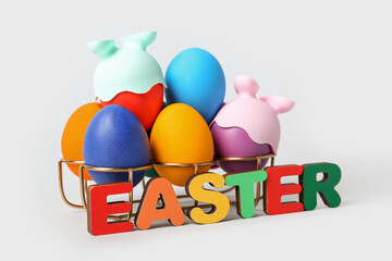 Holder with funny painted eggs and word EASTER on grey background