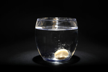 Glass of water with soluble tablet on black background