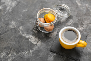 Drink coaster with cup of coffee and macaroons in jar on grey grunge background