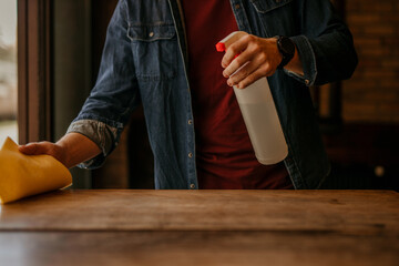 The young man carefully cleaning a table with a sanitizing spray. Focus on hands and spray