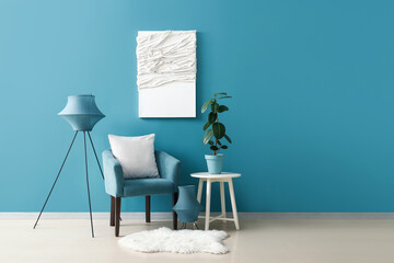 Cozy armchair with cushions, lamp and houseplant on coffee table near blue wall