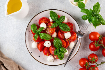Italian caprese salad with sliced tomatoes, mozzarella, basil, olive oil on a light background. Top view. Italian food. Healthy salad. Summer food